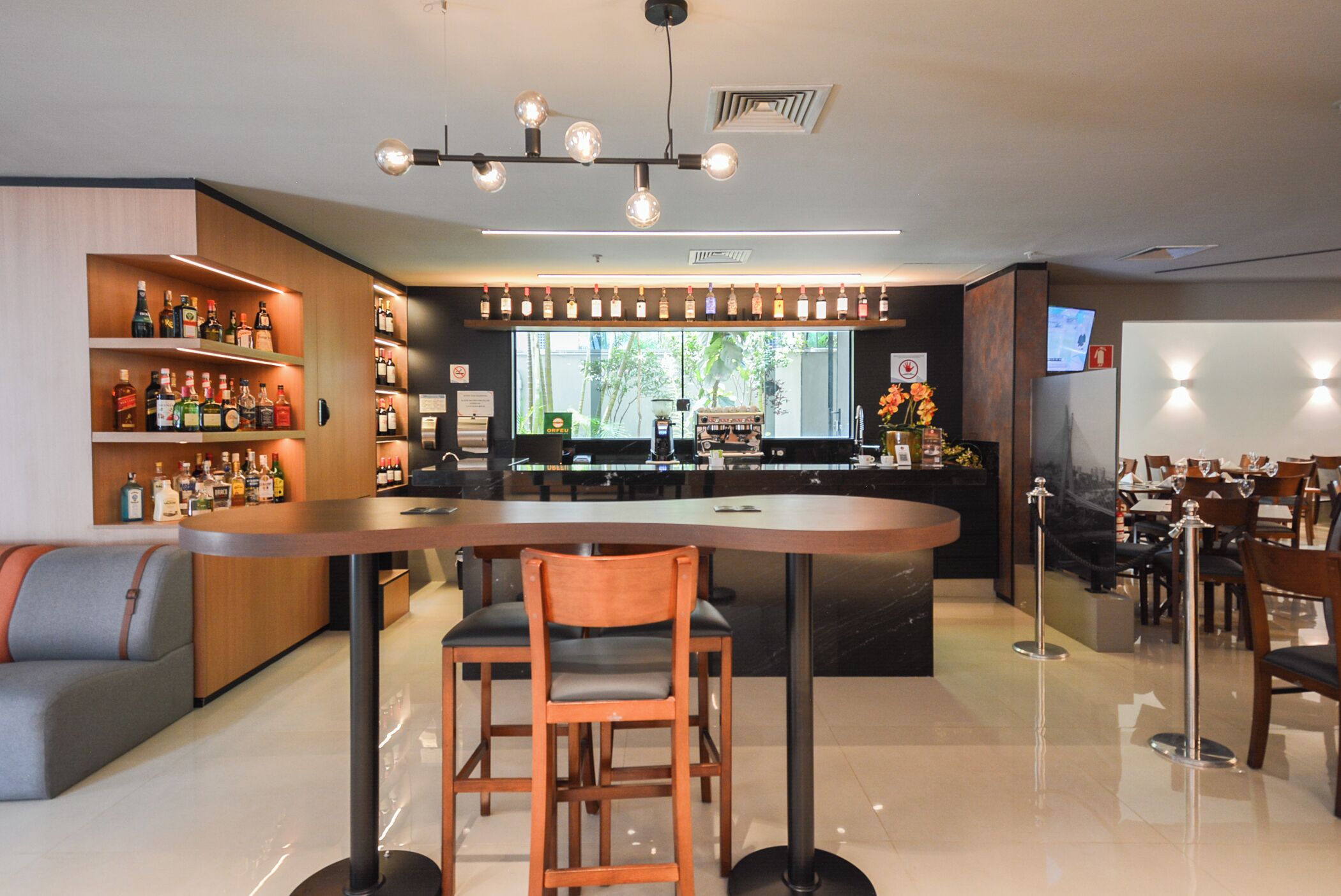 A modern bar area with a long counter, wooden chairs, and shelves of liquor bottles.