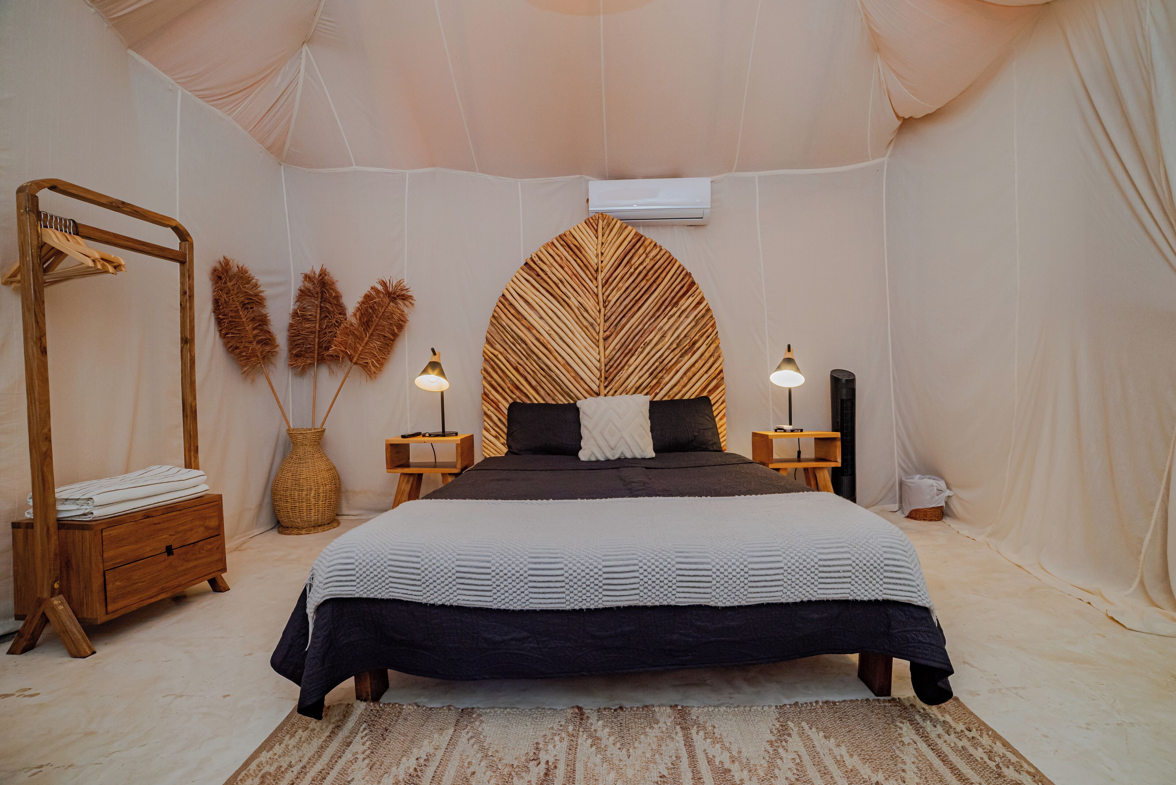 Une chambre à coucher avec un grand lit, une armoire en bois, un fauteuil suspendu et un climatiseur fixé au mur.