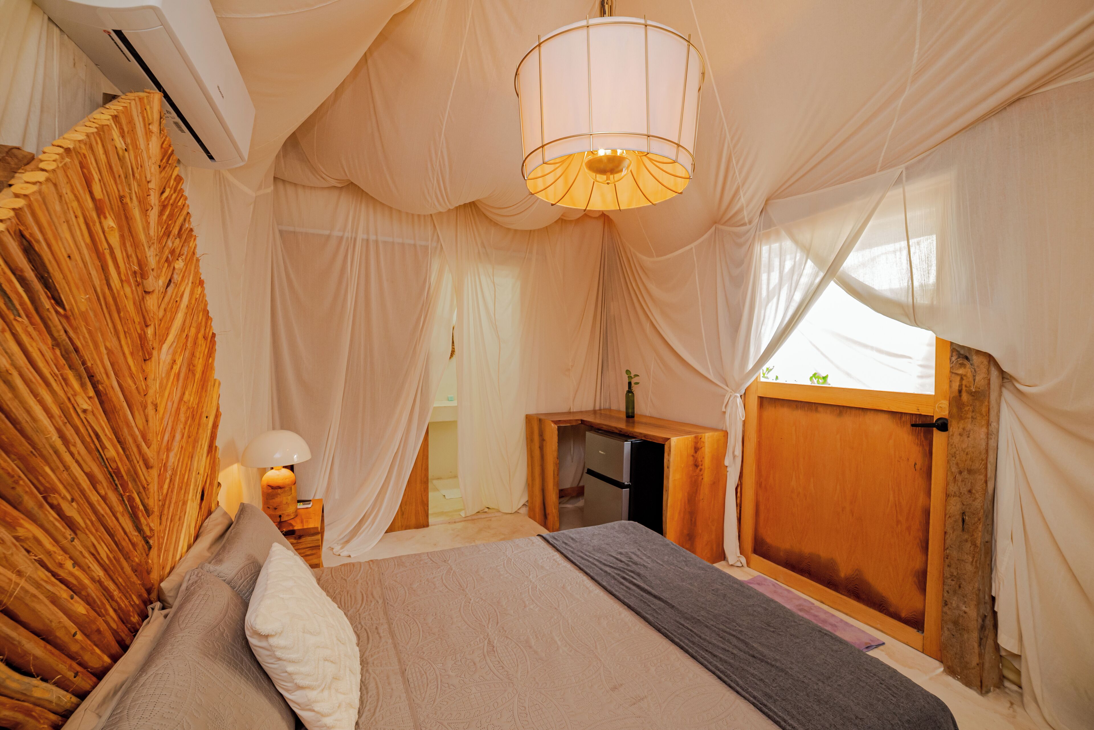 A bedroom with a bed, a bedside table, a lamp, and a wooden desk.