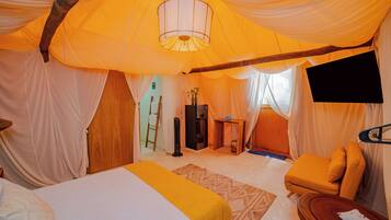 Een tent-achtige kamer met een bed, een klein tafeltje, een stoel en een aan de muur bevestigde televisie.