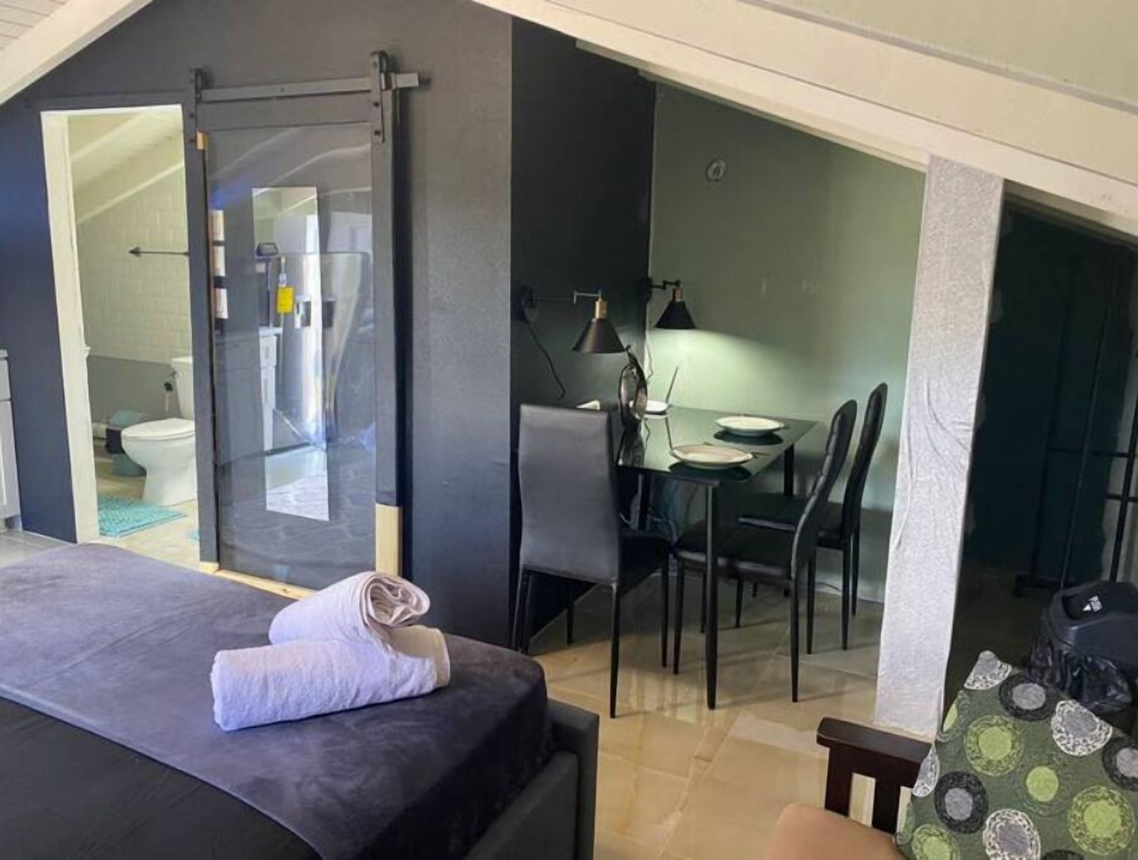 Une chambre avec un lit, une salle de bain avec des toilettes et un coin repas avec une table et des chaises.