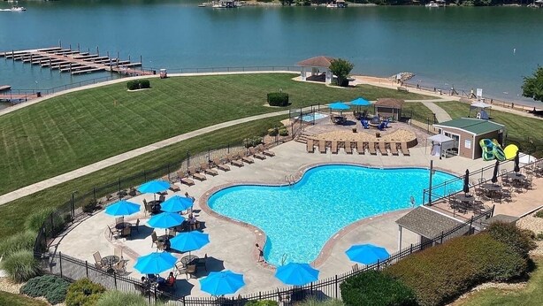 A swimming pool with lounge chairs and umbrellas, surrounded by a fence and a grassy area. - #344 Pointe - 2 Bedroom Lakefront Condo at Mariners SML (Bedford County)
