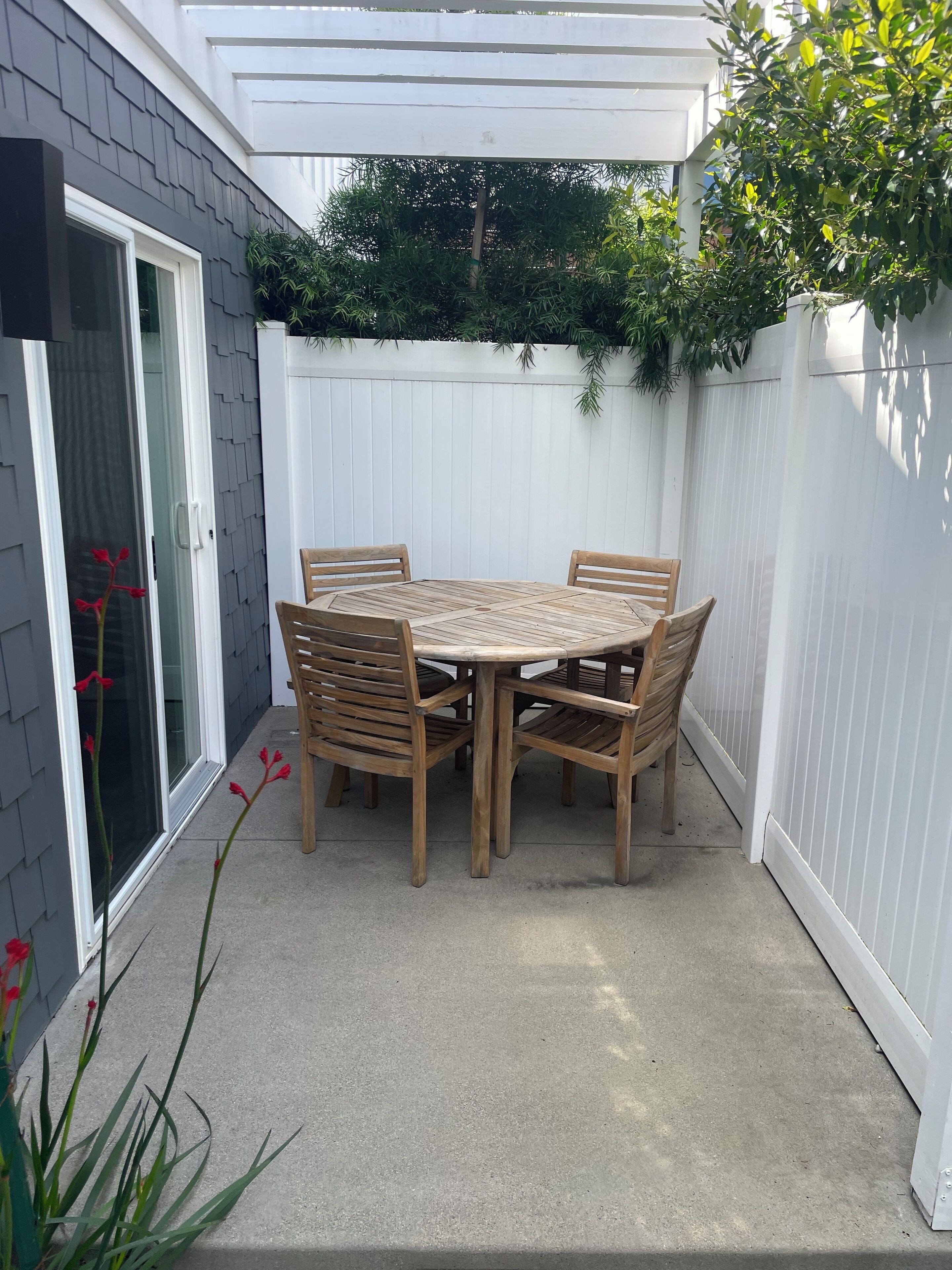 Eine Terrasse mit einem runden Holztisch und Stühlen, einem weißen Zaun und einer Tür mit Fensterteil.