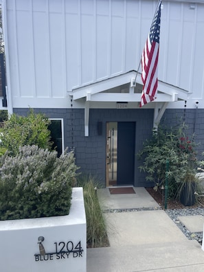 Welcome to 1204 Blue Sky Dr, where a beautifully maintained garden leads to a stylish entrance with a glass door and American flag.