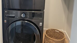 Una lavadora y secadora apiladas con un panel de control, una cesta y un estante blanco con una caja.