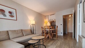 Een moderne woonkamer met een bank, twee bijzettafeltjes en een eethoek met stoelen en een lamp.
