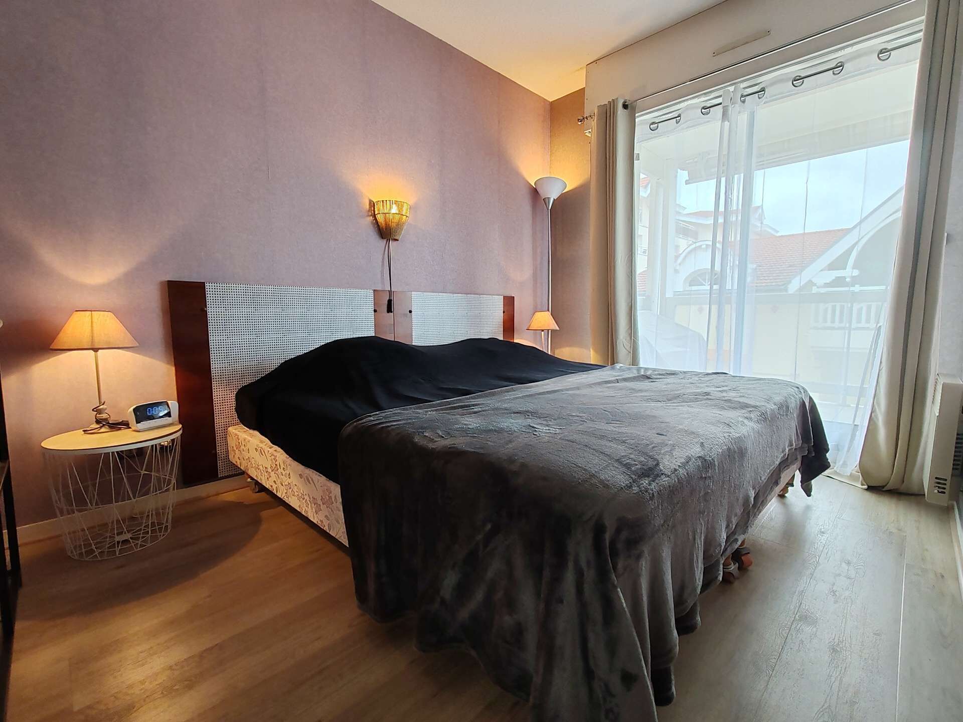 Een hotelkamer met een bed, bedlampjes, een digitale klok en een raam met gordijnen.