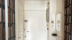 Een hal met een witte deur, houten vloer, een zwarte prullenbak en boekenplanken aan weerszijden.