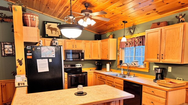 A kitchen with wooden cabinets, a refrigerator, a microwave, an oven, a sink, and a bar area with stools.
