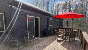 A wooden deck with outdoor furniture, a red umbrella, and a cabin with a sliding glass door.