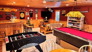 A cozy bar area with a foosball table, pool table, and various seating options.