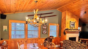 A wooden interior with a dining table, chairs, a bear statue, and a fireplace.