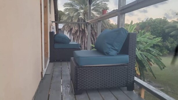 Un balcone con due poltrone in vimini e un tavolino, affacciato su un giardino con palme e vista sul cielo.