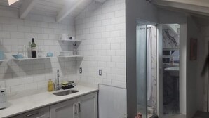 Una cucina moderna con piastrelle bianche stile metro, un lavello in acciaio inossidabile e un box doccia in vetro.