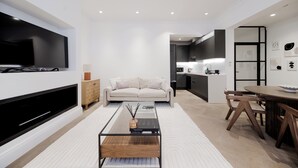 Ett modernt vardagsrum med en platt-TV, en soffa, ett soffbord och en matplats med trästolar och ett bord.