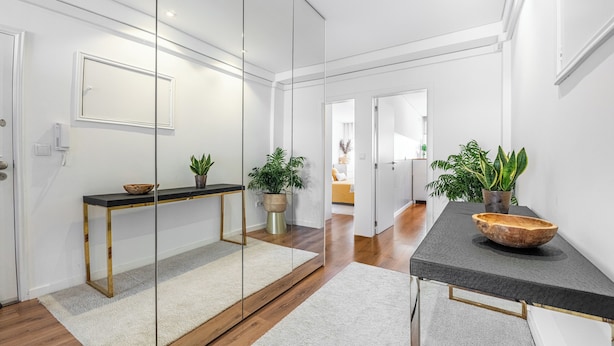 Een modern interieur met een houten vloer, een zwarte console tafel, een wit tapijt en potplanten.