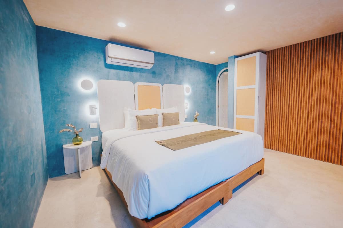 A bedroom with a large bed, bedside tables, a wall-mounted air conditioner, and a wooden panel wall.