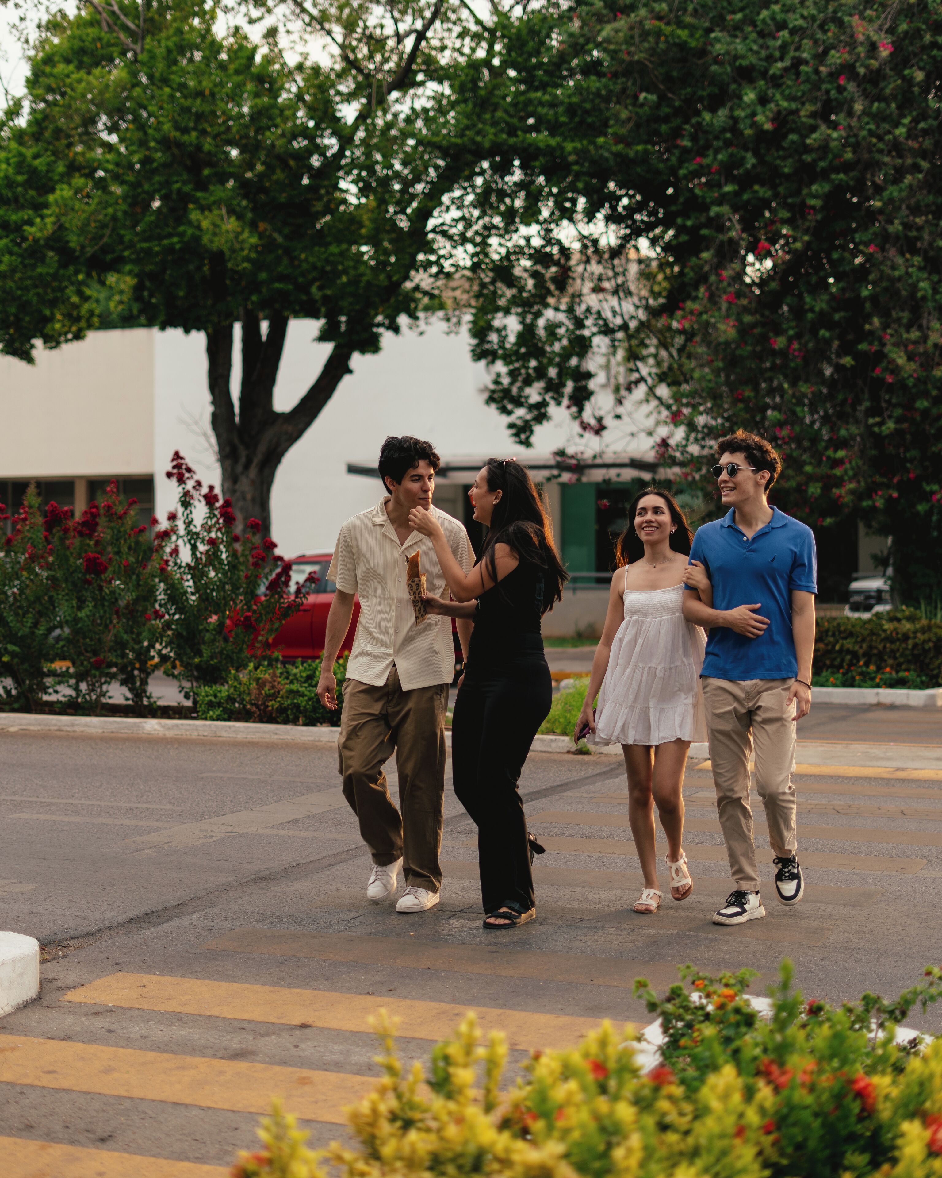 A group of people walking on a street with trees and a building in the background.