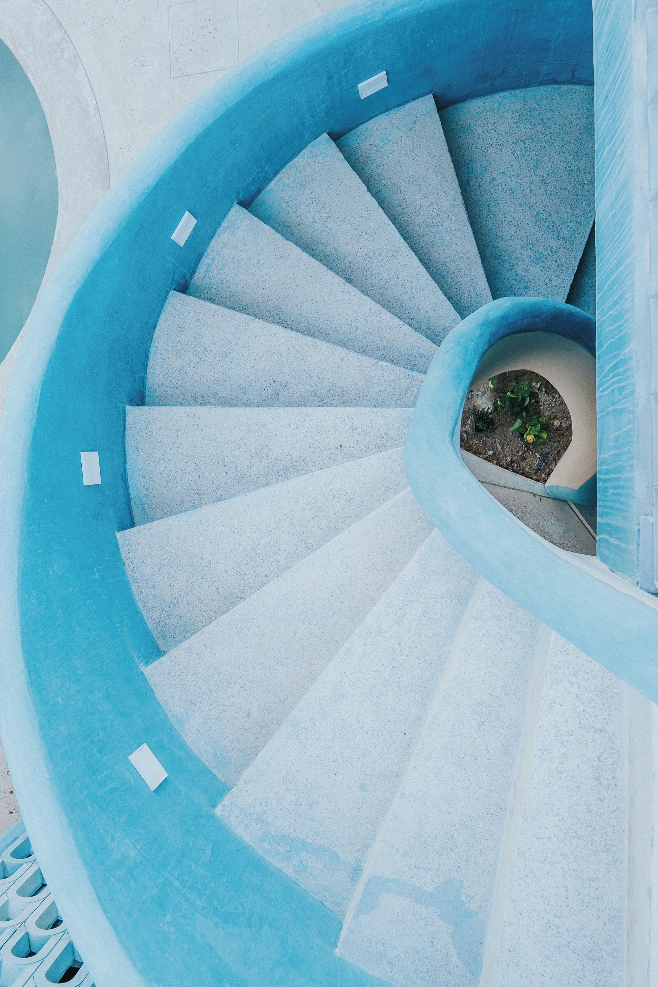 A spiral staircase with blue steps and a small garden area at the bottom.
