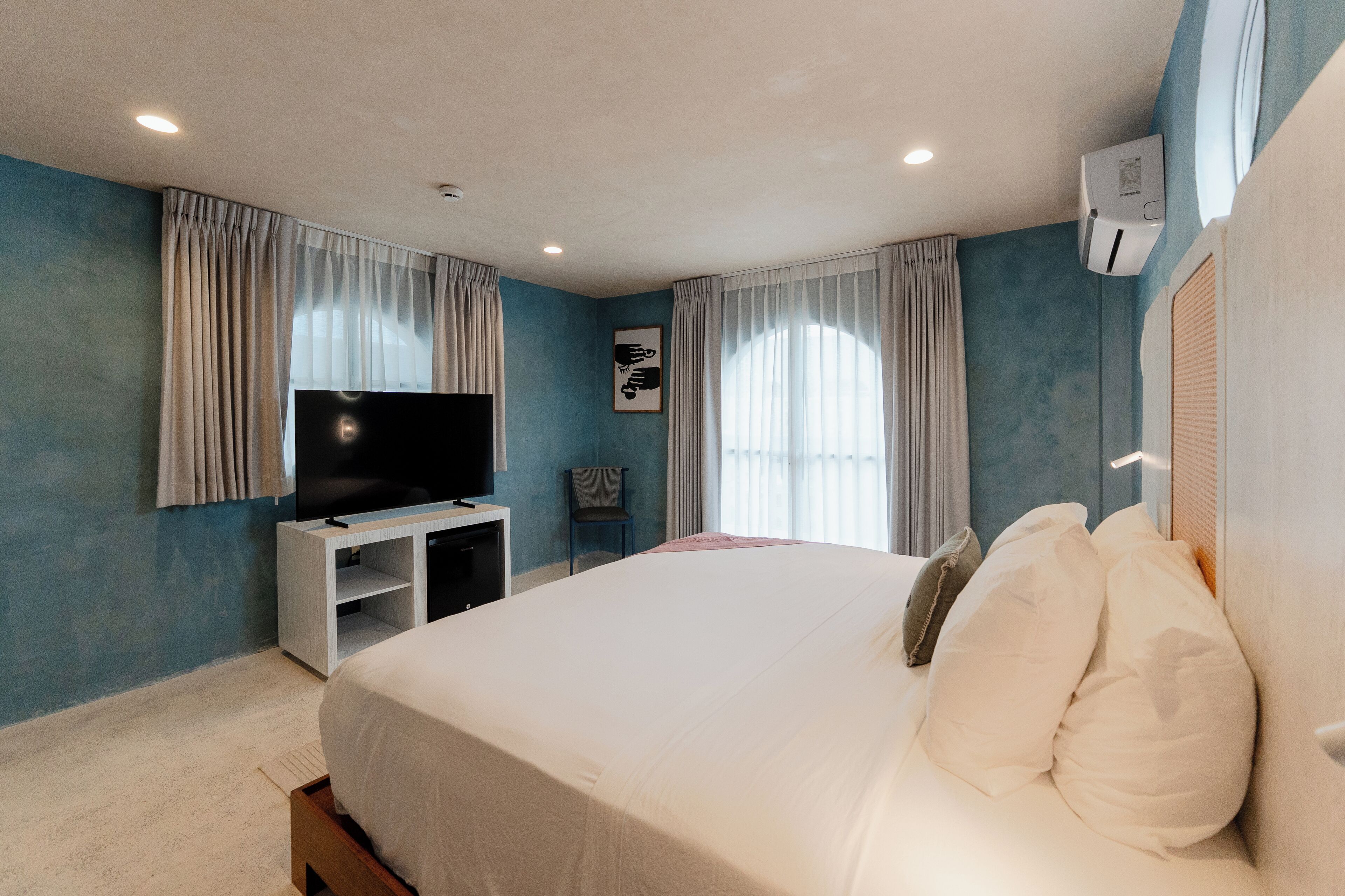 Ein Hotelzimmer mit Bett, Fernseher auf einem Schrank, einem Sessel und einem Fenster mit Vorhängen.