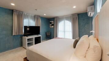 A hotel room with a bed, a TV on a stand, a chair, and a window with curtains.