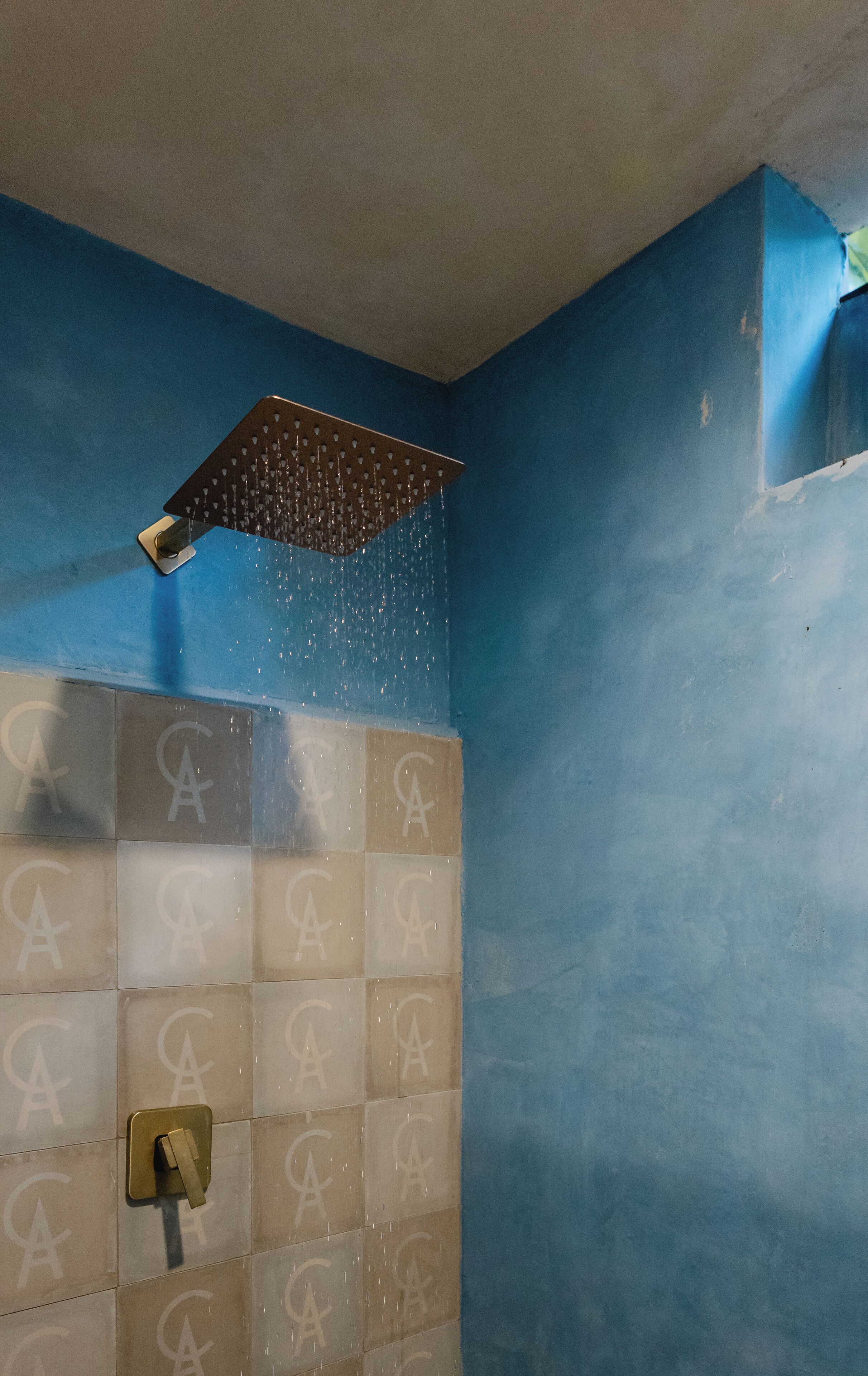 A shower with a square showerhead and a tiled wall with a repeating pattern.