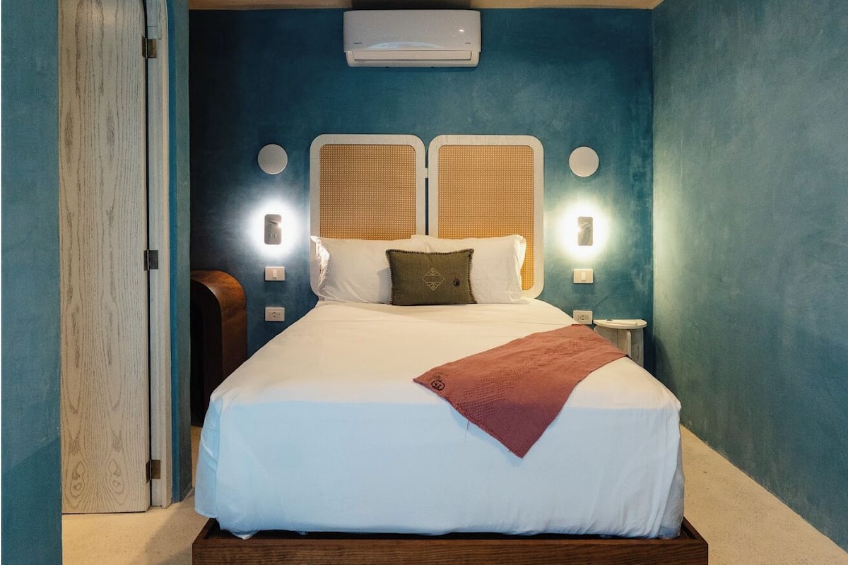 A bedroom with a large bed, two wall-mounted lights, and an air conditioning unit.