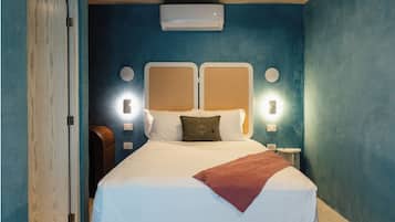 Une chambre avec un grand lit, deux lampes fixées au mur et un appareil de climatisation.