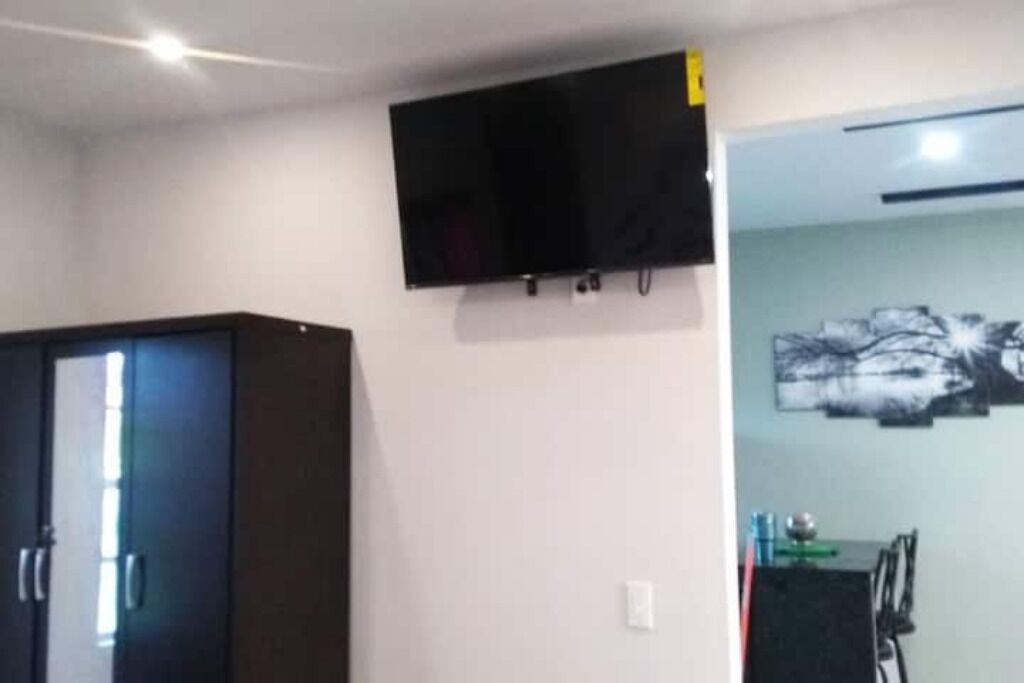 Ett rum med en mörk garderob, en väggmonterad platt-TV och en matplats med ett bord och stolar.