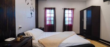 A bedroom with a bed, bedside table, wardrobe, and two windows with curtains.