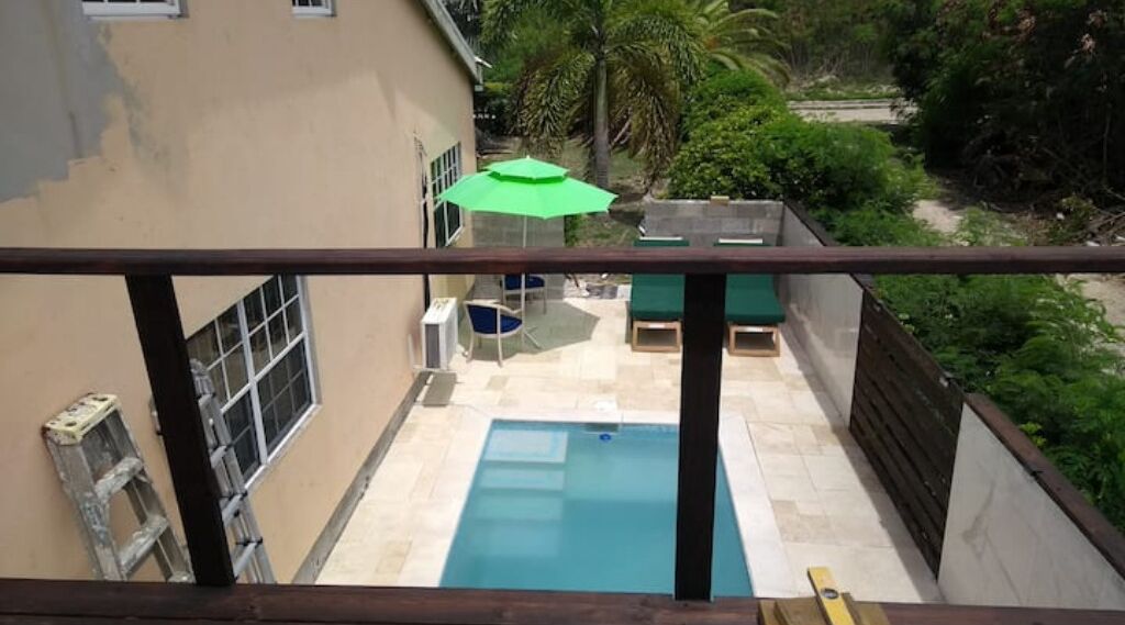 A swimming pool with a green umbrella, a ladder, and outdoor furniture.