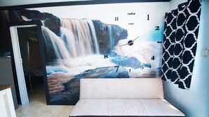 Ein Zimmer mit einer großen Wandmalerei eines Wasserfalls, einem Sofa und einem gemusterten Vorhang.