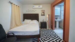 Ein Schlafzimmer mit einem Bett, einem Nachttisch, einer wandmontierten Klimaanlage und einem durchgehenden Türrahmen einsehbaren Badezimmer.