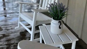 Un portico coperto con mobili in legno bianco, tra cui una panca e un tavolino. Sul tavolo, un vaso con lavanda.