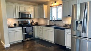 Una cucina moderna con mobili bianchi, elettrodomestici in acciaio inossidabile e un'ampia finestra con persiane.