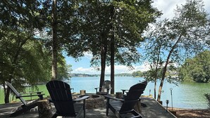 A lakeside seating area with Adirondack chairs and a stone fire pit.