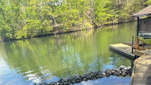 A wooden dock extending over a calm lake, surrounded by lush greenery and a stone barrier.