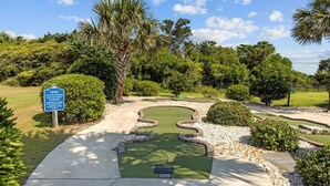 Un parcours de golf doté d’un green d’entraînement, entouré d’une végétation luxuriante et de palmiers.