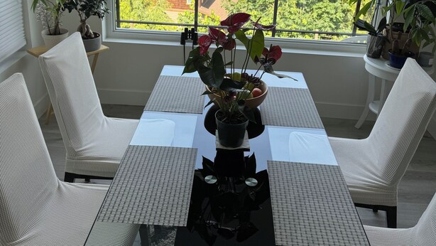 A dining area with a table and chairs, a hanging light fixture, and a view of a lake and forest through a large window. - Vacation home in Sechelt (Sechelt)