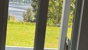 A room with a large window overlooking a grassy area and a body of water. - Vacation home in Sechelt (Sechelt)