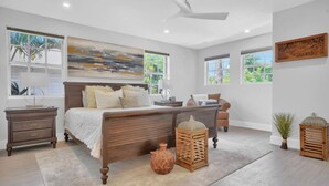 Een slaapkamer met een groot bed, een nachtkastje, een lamp, een vaas en een raam met uitzicht op groen.