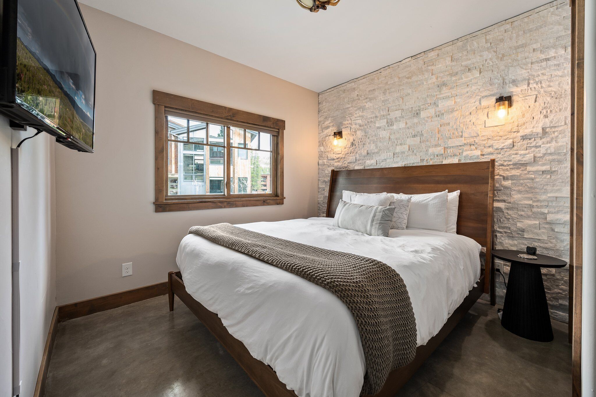 Un dormitorio con una cama grande, una ventana, una pared de piedra y un televisor montado en la pared.