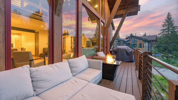 Una terraza de madera con un sofá y un brasero, con vistas a una zona residencial con casas y árboles.