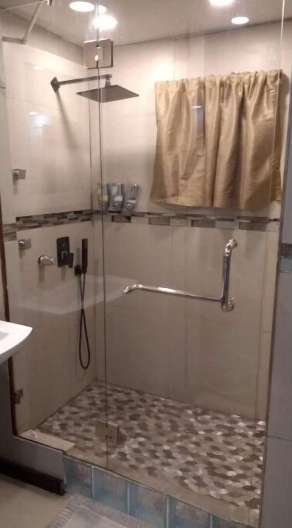 A glass-enclosed shower with a handheld showerhead, a handheld showerhead, and a wall-mounted faucet.