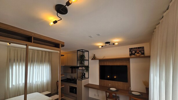 Un espacio habitable compacto con kitchenette, zona de comedor y televisor montado en la pared.