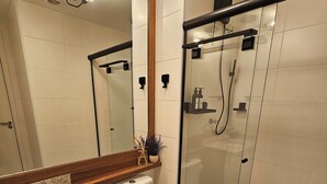 Un baño moderno con cabina de ducha de vidrio, inodoro y lavamanos con encimera de madera.