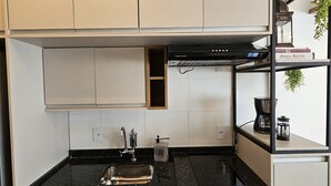 Una cocina compacta con encimera negra, estufa integrada y microondas. Hay armarios arriba y abajo del mostrador, y un pequeño estante con una planta y un libro.