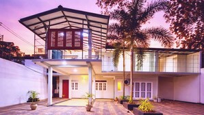 A two-story house with a covered balcony, potted plants, and a paved courtyard.