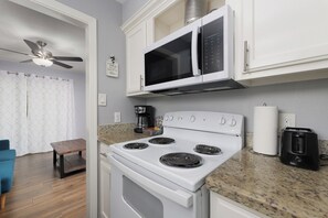 Compact kitchen with a stove, microwave, and toaster, adjacent to a cozy living area with a table and chair.