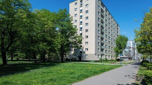 A multi-story building with a flat facade, surrounded by a park with green grass and trees.